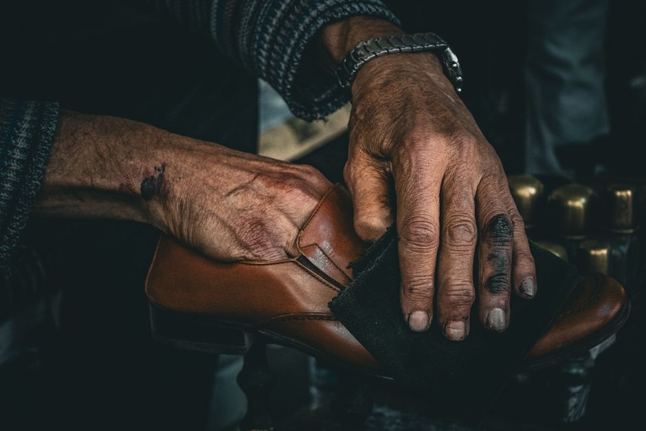 Detailed image of hands polishing a leather shoe, showcasing craftsmanship and tradition.