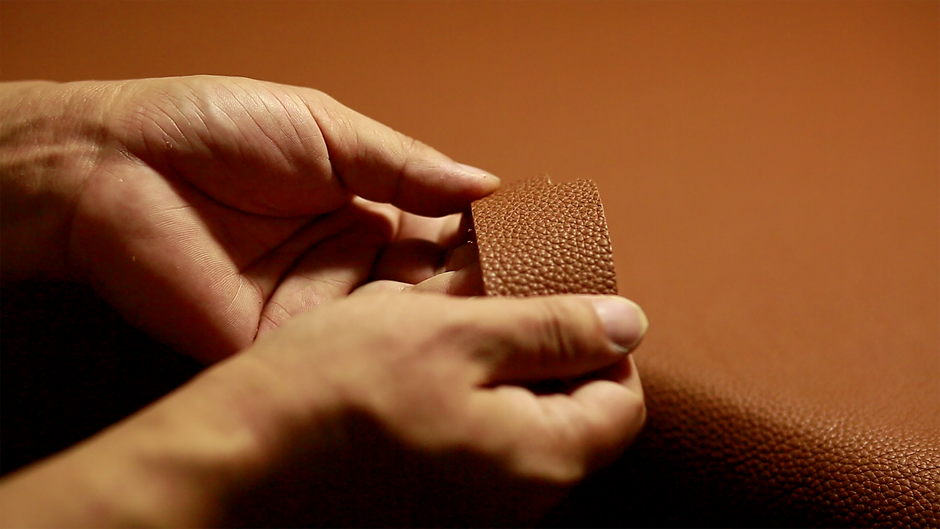 Detailed close-up of hands holding and examining textured brown leather material.