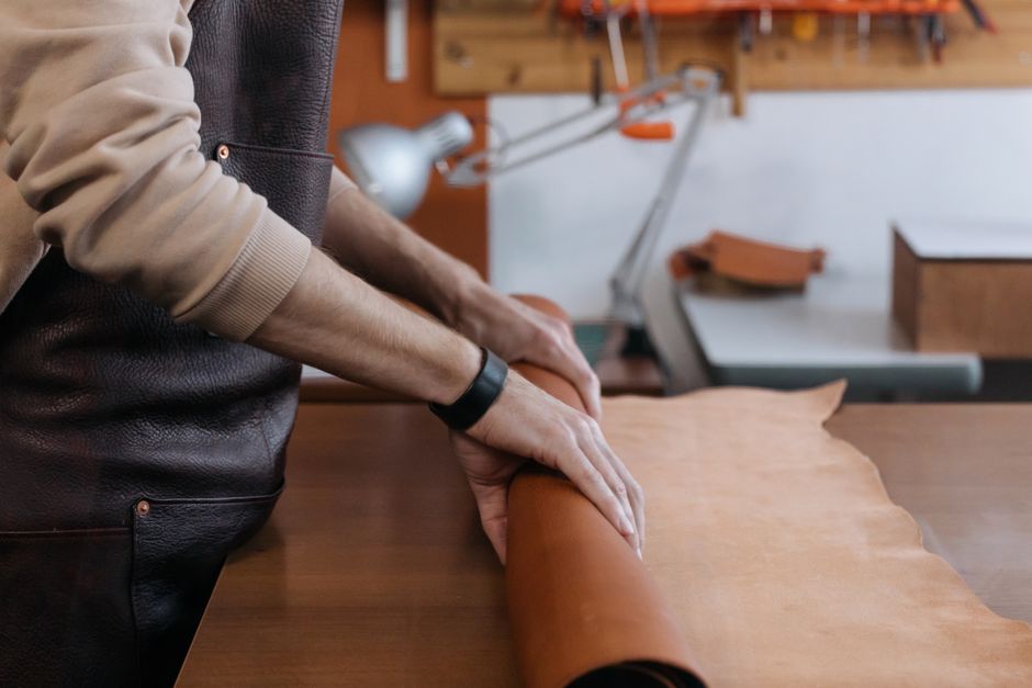 Close-up of hands rolling leather in a workshop setting, perfect for leathercraft themes.